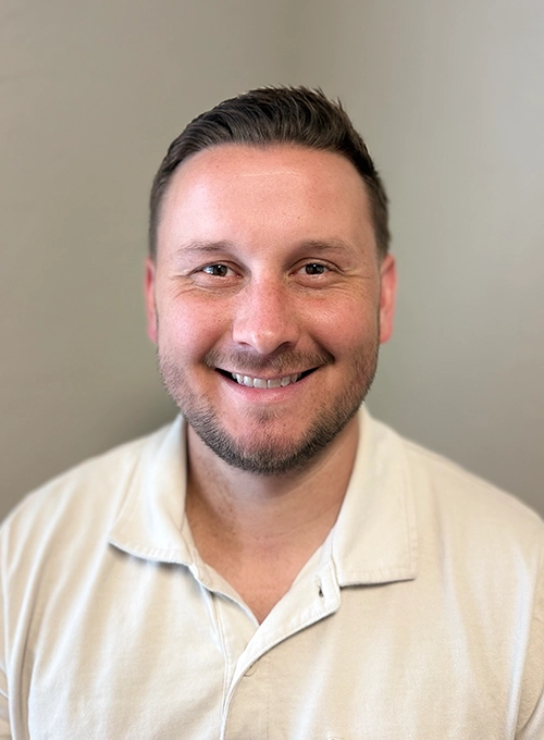 Chiropractor Joshua Harvey Smiling In Collared Shirt In Front Of Beige Background
